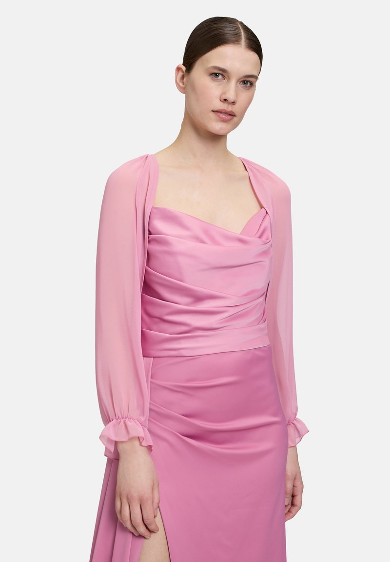 Robe rose avec un corsage drapé et une fente haute, complétée par un boléro en tulle à manches bouffantes. Tissu lisse avec une texture douce.
