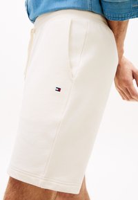 Μπεζ βαμβακερά σορτς με πλαϊνές τσέπες, ελαστική μέση και μικρό κεντημένο λογότυπο. Ομαλή υφή και μήκος μέχρι το γόνατο.