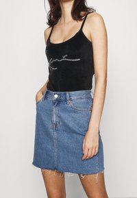 Svart sammetstopp med silvriga rhinestone-detaljer, kombinerat med en ljusblå denimkjol med fransar och framfickor.