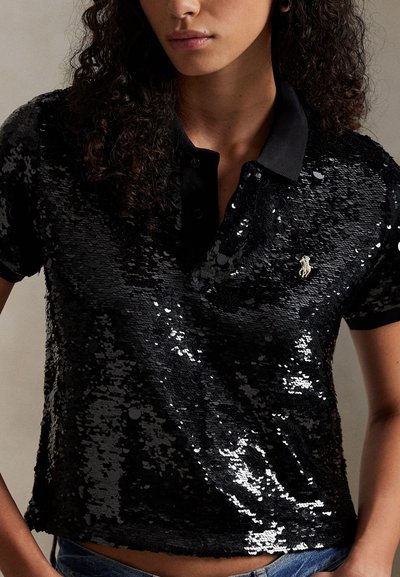 Črna polo majica s kristalčki, črnim ovratnikom in gumbi, z majhnim vezenim logotipom na prsih. Gladek tekstura in oprijeta zasnova.
