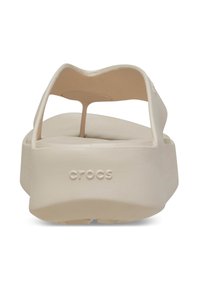 Sandali Crocs beige con finitura liscia, suola a piattaforma ampia, fasce sottili e una leggera curvatura nel design superiore. "CROCS" stampato sul lato.