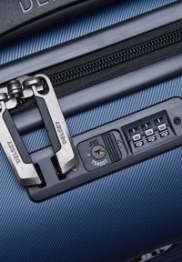 Maleta dura azul con acabado texturizado, que cuenta con doble cremallera de metal, un candado aprobado por la TSA y una cerradura de combinación en el lateral.