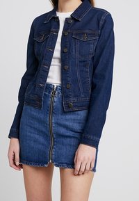 Mörk denimjacka med två framfickor, knäppning med knappar och krage, i kombination med en matchande blå kjol med dragkedja fram.