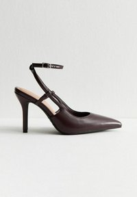 Tacco a rocchetto in finta pelle marrone con punta affilata, cinturino alla caviglia e design con ritagli. Tacco di 4 pollici con texture liscia e hardware minimo.