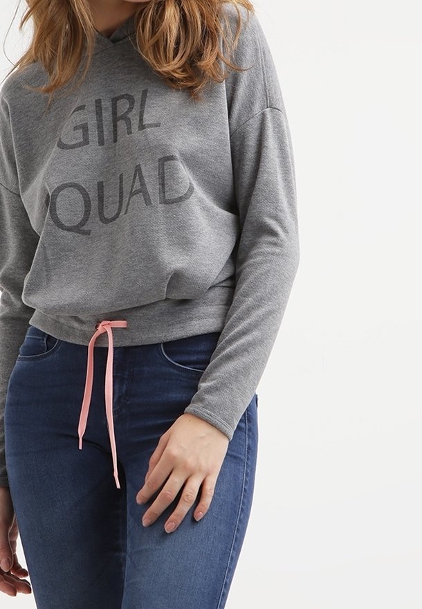 Sudadera gris con capucha y las palabras "GIRL" y "SQUAD" impresas en letras oscuras. Cuenta con un cordón rosa en la cintura, combinado con jeans azules.