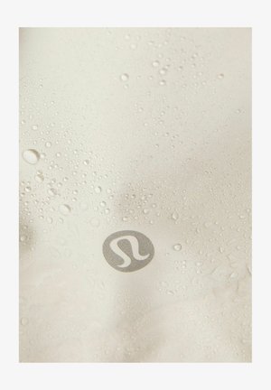 Voděodolná tkanina ve světle béžové barvě s viditelnými kapkami vody. Obsahuje stříbrné logo v pravém dolním rohu. Hladká textura.