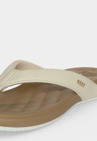 Tongs Reef beige et marron avec bride texturée et semelle intérieure coussinée et moulée sur fond blanc.