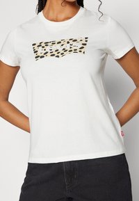 Bílý bavlněný tričko s béžovým a černým leopardím potiskem loga Levi's. Klasický design s kulatým výstřihem, krátkými rukávy a rovného spodního lemu.