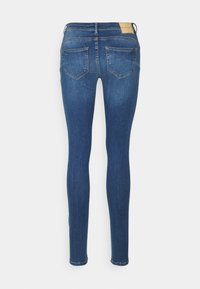Calças skinny em denim azul escuro com uma textura suave. Apresentam uma costura em yoke, dois bolsos traseiros e um patch com o logótipo acima do cós.