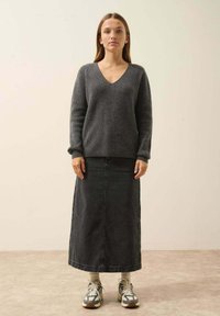 Szary sweter z dzianiny w serek. Połączony z czarną długą spódnicą z dżinsu i szarymi trampkami z wielokolorowymi akcentami.