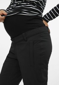 Pantalons de maternité noirs avec une taille extensible, texture lisse et poches latérales, associés à une chemise rayée noir et blanc.