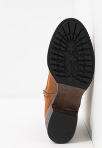 Botte en daim marron avec une semelle en caoutchouc noir texturé, présentant un motif de semelle détaillé et une légère usure au niveau du talon. Taille 37.