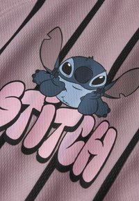 Roosa kangas, millel on joonistus multikategelaskest, kellel on suured kõrvad ja silmad, ning prinditud tekst "STITCH" ja mustad vertikaalsed triibud.