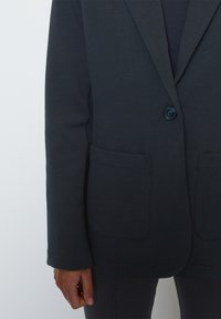 Dark grey blazer made of soft fabric, featuring a single button closure, two front pockets, and a tailored fit with a smooth texture.