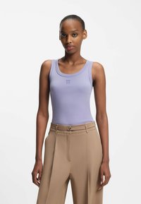 Lilaaninsävyinen, vartalolle istuva toppi pyöreällä p�ääntiellä, jossa on hillitty "HUGO"-logo. Yhdistetty korkeavyötäröisiin beigen värisiin housuihin, joissa on vyöhön liittyvä yksityiskohta.