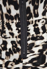 Tissu animalier noir et blanc avec texture froncée, doté d'une fermeture éclair noire au centre. Matériau lisse et extensible.