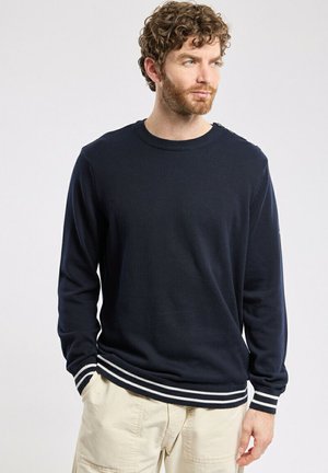 Pull en tricot marine avec un col rond, des manches longues et des poignets et un ourlet côtelés à rayures blanches. Texture lisse sans motifs visibles.