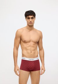 Czerwone slipy męskie Calvin Klein z geometrycznym wzorem, elastycznym paskiem z logo oraz dopasowanym fasonem, wykonane z miękkiego materiału tekstylnego.