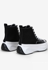 Sneakers neri alti con lacci bianchi, suole bianche e cuciture a contrasto. Presentano una tomaia in tessuto texturizzato e un collo imbottito.