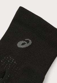 Calcetín atlético negro hecho de tela texturizada, con un logo gris. El diseño incluye patrones de ventilación para una mayor transpirabilidad.