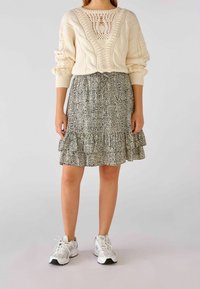 Strik creme sweater med teksturerede mønstre og et udskåret design, kombineret med et sort-hvidt mønstret flæsekjol, båret med grå sneakers.