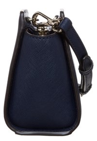 Sidorna av en marinblå texturerad handväska med svarta kanter, guldfäste och en justerbar rem som är fäst med en metallring.