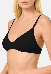 Sostén triangular negro con tirantes delgados y ajustables y una textura suave. Diseño simple con un escote pronunciado y sin herrajes visibles.