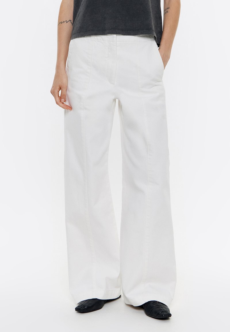 Pantalones de pierna ancha blancos, hechos de denim de algodón, que cuentan con bolsillos frontales, costuras visibles y un diseño de cintura alta.