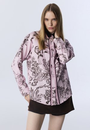 Chemise à manches longues en tissu rose avec un imprimé floral noir complexe et des motifs abstraits, dotée d'un col et d'une fermeture à boutons sur le devant.