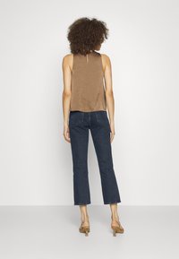 Top marrón sin mangas con un escote tipo ojal en la parte posterior, combinado con jeans recortados de color azul oscuro. Los zapatos son claros con una textura sutil y un tacón cuadrado.