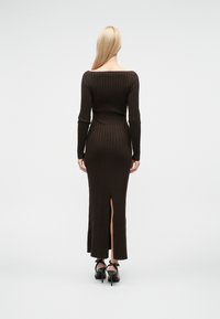 Brun ribbestrikket kjole med lange ermer, rund hals og sidespalt. Brukt med svarte høyhælte sko. Glatt tekstur.