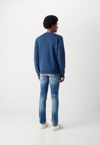 Felpa blu navy con collo rotondo e polsini a costine, abbinata a jeans chiari e sneakers bianche, vista da dietro.