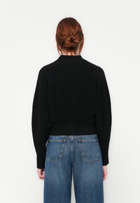 Svart ribbet genser med høy hals og vidde ermer, kombinert med middels høye blå jeans med subtil falming og klassiske baklommer.