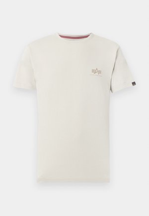 Μπεζ T-shirt με κοντά μανίκια, με μικρό λογότυπο Alpha Industries στο αριστερό στήθος και μια μικρή μαύρη ετικέτα στο αριστερό μανίκι.