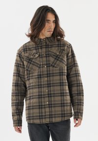 Een geruite shirt gemaakt van textuurstof in aardetinten van bruin en zwart, met borstzakken en een knoopsluiting aan de voorkant met afgeronde zoom.