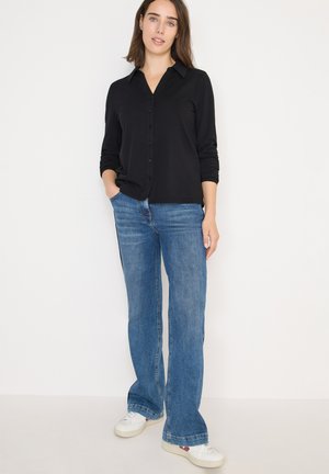 Zwarte button-up shirt met lange mouwen, gecombineerd met blauwe flared jeans en witte sneakers. Eenvoudig ontwerp, casual pasvorm.