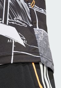 Czarna tkanina sportowa z graficznym wzorem w białe i pomarańczowe akcenty. Logo "AEROREADY" znajduje się w pobliżu dołu. Gładka tekstura.