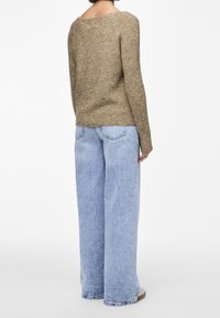 Pull en tricot texturé marron associé à un jean bleu clair à jambes larges, caractérisé par une coupe décontractée et un col rond.