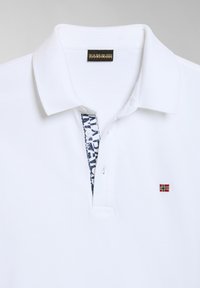 Polo bianco in cotone, con una patta decorata e una piccola bandiera norvegese ricamata sul petto.