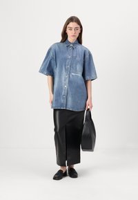 Υπερμεγέθής τζιν πουκάμισο με κοντά μανίκια, ανοιχτό μπλε χρώμα, μπροστινή τσέπη, συνδυασμένο με μαύρη δερμάτινη φούστα με σχίσιμο και μαύρες λουστρίνια.