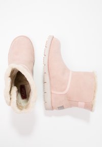 Paire de bottes d'hiver en suède rose avec une doublure en fausse fourrure couleur crème, une botte vue de dessus et l'autre de côté sur fond blanc.