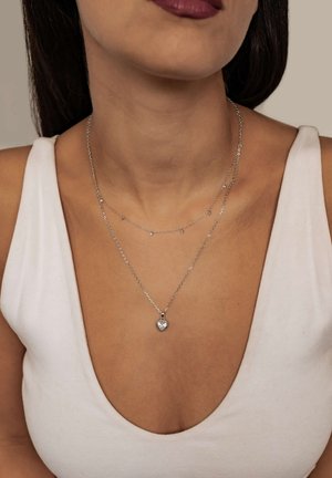 Silberne Schichtketten bestehen aus einem Herzanhänger mit einem klaren Edelstein, zarten Kettengliedern und kleinen Akzentsteinen an der oberen Kette.