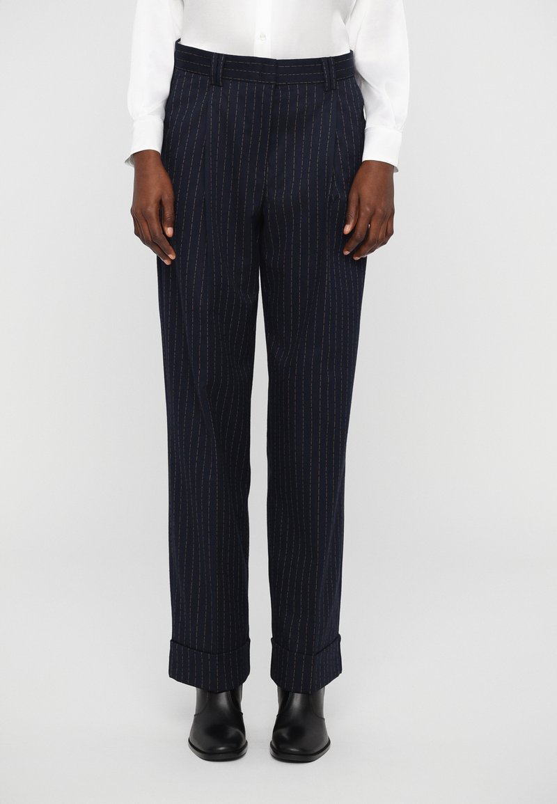 Navy trousers with pinstripes, featuring a pleated front, cuffed hems, and a smooth, textured finish. Worn with a white button-up shirt.