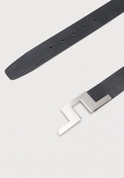 Μαύρη δερμάτινη ζώνη με ασημένια αγκράφα σε γωνιώδη σχήμα ζιγκ-ζαγκ και πέντε τρύπες ρύθμισης σε σχήμα κλειδαρότρυπας σε ανοιχτό φόντο.