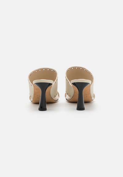 Beige hoge hakken mules met een gladleren bovenkant, voorzien van metalen studs en zwarte stilettokoppen. Ontwerp met open achterkant.