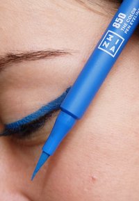 Ljusblå eyelinerpenna med fin spets, applicerad längs franslinjen. Omgivande hud visar en lätt struktur och ögonbrynshår syns ovanför ögat.