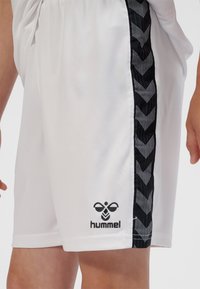 Weiße Sportshorts mit einem schwarzen Chevron-Muster an der Seitenstreifen und einem schwarzen Logo unten links, gefertigt aus leichtem Material.