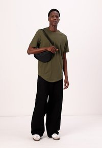 Tricou din bumbac de culoare verde măsliniu, geantă de umăr neagră, pantaloni largi negri, adidași de culoare deschisă. Design simplu, croi lejer, textură fină.