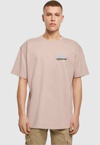 Lys rosa bomulds t-shirt med korte ærmer. Har et lille sort logo på venstre bryst og en afslappet, oversized pasform.