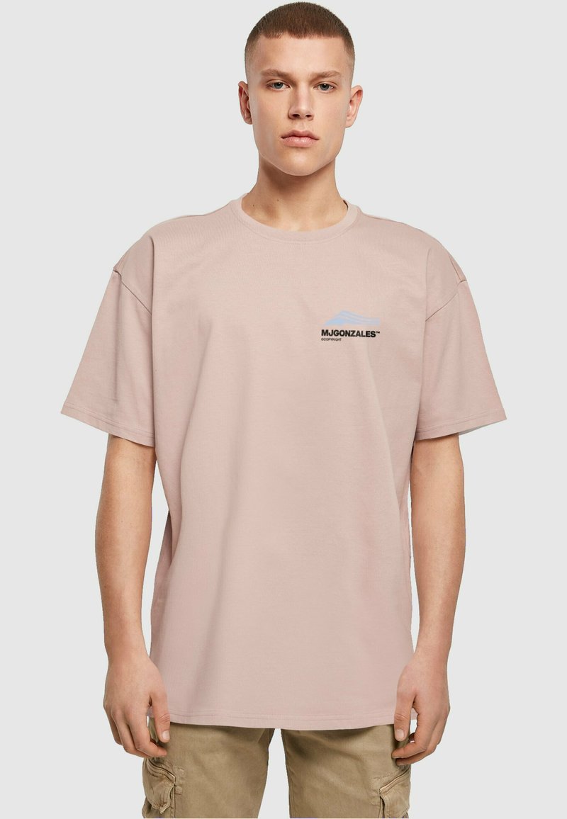 Lys rosa bomulds t-shirt med korte ærmer. Har et lille sort logo på venstre bryst og en afslappet, oversized pasform.